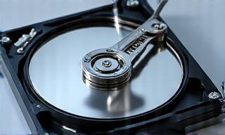 Hard disk aperto per recupero dati, con un braccio robotico che maneggia il piatto magnetico in sala bianca.